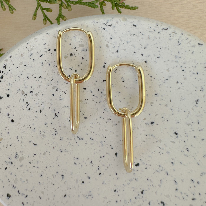 A pair of 14k gold filled double oval link hoop earrings on a marble surface.