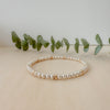A gold-filled and silver beaded bracelet with a mix of round and rondelle shaped beads, displayed on a wooden surface next to some green leaves for a decorative touch.