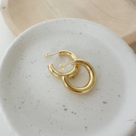 A pair of gold-filled hoop earrings placed on a white ceramic dish.