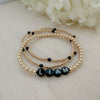 A bracelet with black and white beads, featuring the name 'Liam' in white letters on black beads, displayed on a wooden surface with a flower in the background.