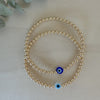 A gold-filled bracelet with a series of uniform beads and a glass bead with a blue evil eye design, strung on a high-quality elastic cord.