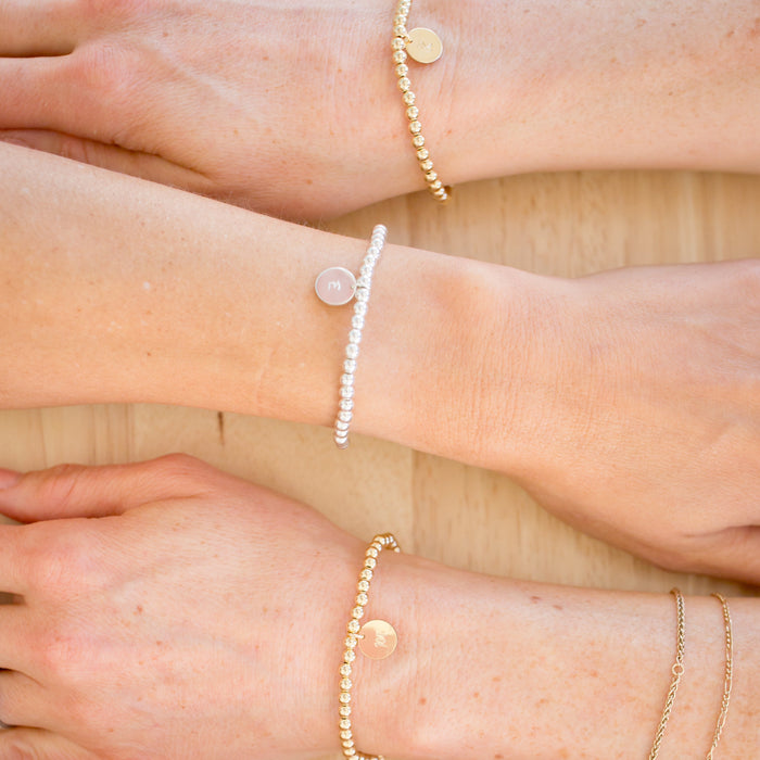 Close-up of hands wearing multiple beaded bracelets on a neutral background