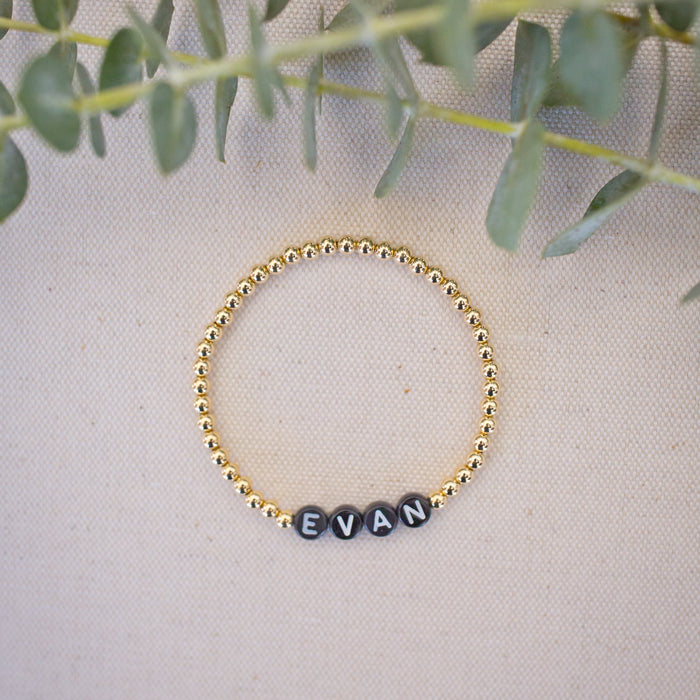 Gold bracelet with engraved name on a light background with green leaves