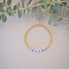 Gold beaded bracelet with name 'Ella' on a beige fabric background