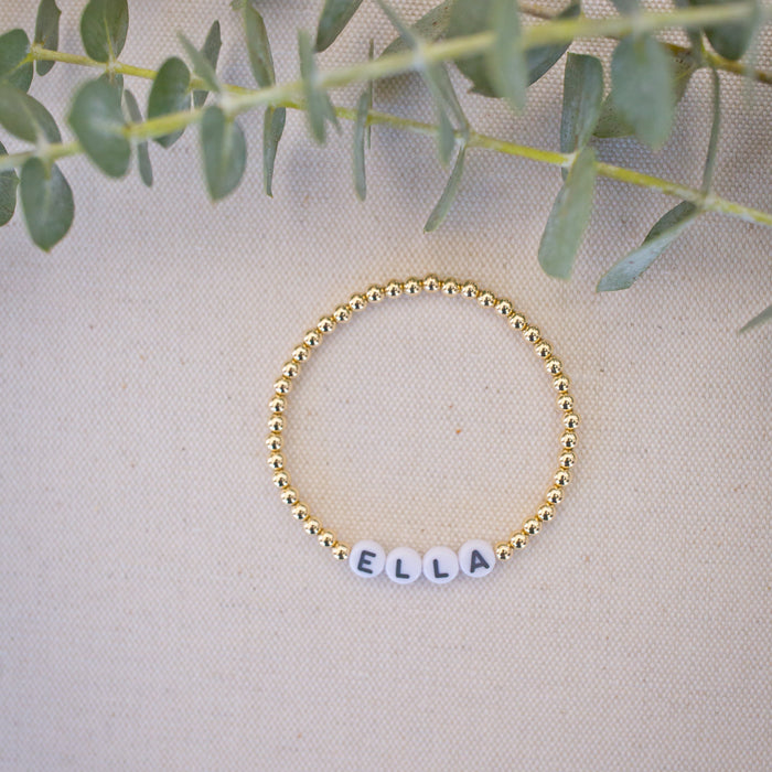 Gold beaded bracelet with name 'Ella' on a beige fabric background