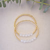 Two beaded bracelets on a light fabric background with green leaves.