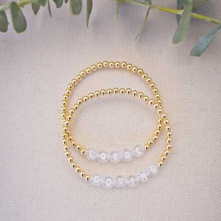 Two beaded bracelets on a light fabric background with green leaves.