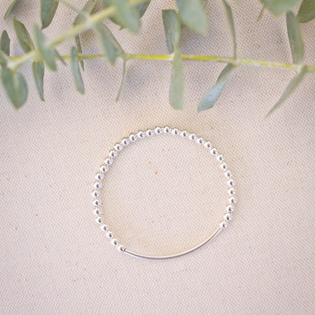 Silver beaded bracelet on a light fabric background with green leaves.