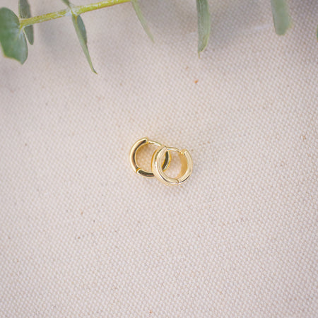 Two gold rings on a textured beige surface with green leaves in the background