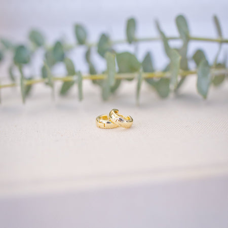 Two gold rings on a white surface with green leaves in the background