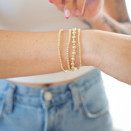 Gold bracelets on a person's wrist with a blurred background