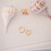 Gold hoop earrings with seashells on a sandy surface
