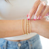 Close-up of a person wearing gold beaded bracelets on a blurred background