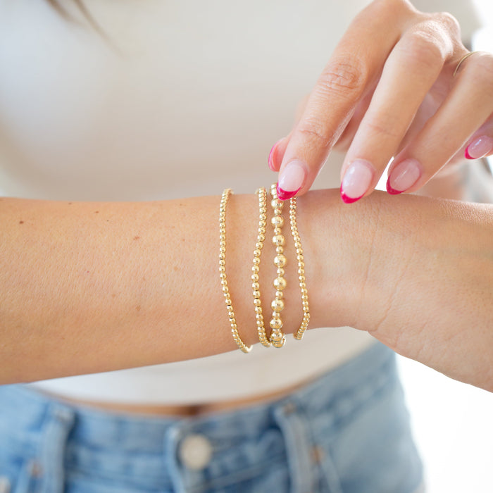 Close-up of a person wearing gold beaded bracelets on a blurred background