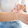Person wearing two gold bracelets on a blurred background
