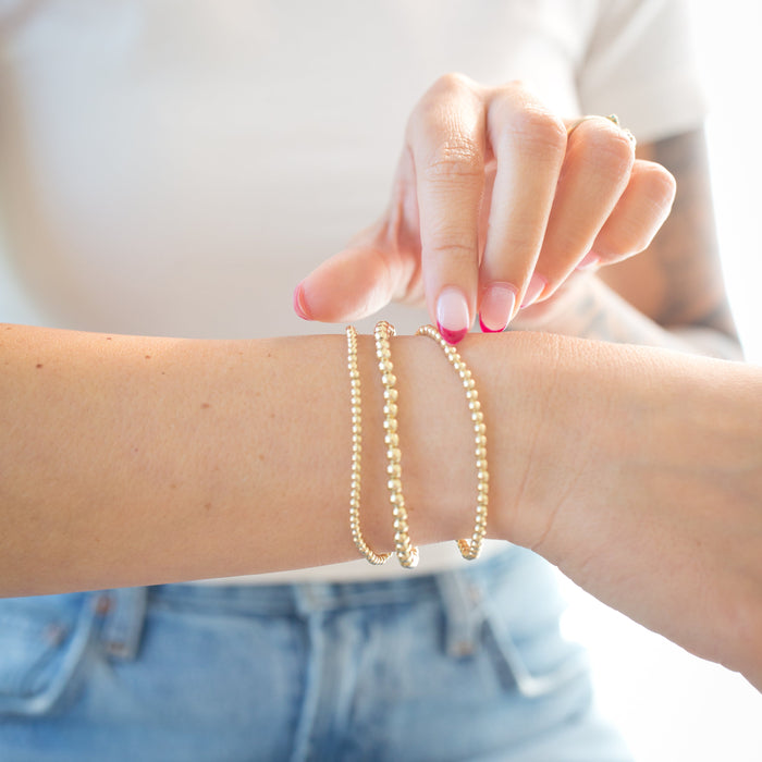 Person wearing two gold bracelets on a blurred background