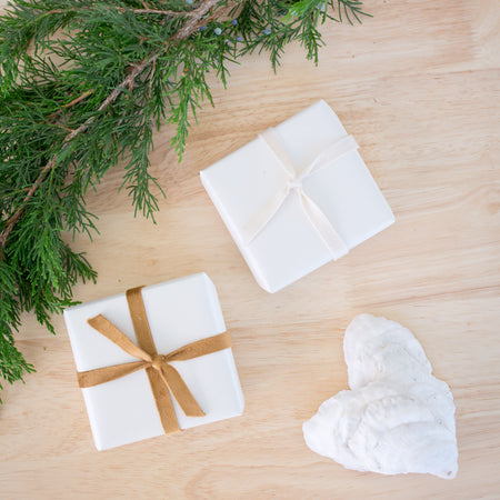 White soap bars with a brown ribbon and greenery on a wooden surface