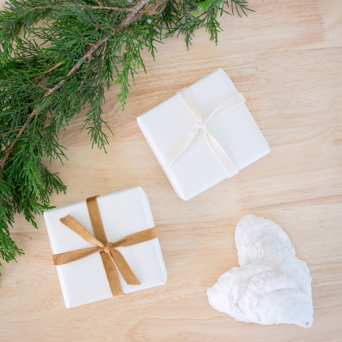 White soap bars with a brown ribbon and greenery on a wooden surface