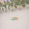 Gold hoop earrings with turquoise stones on a textured surface with greenery in the background