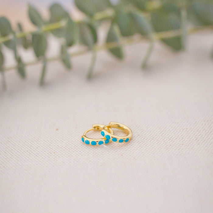 Gold hoop earrings with turquoise stones on a textured surface with greenery in the background