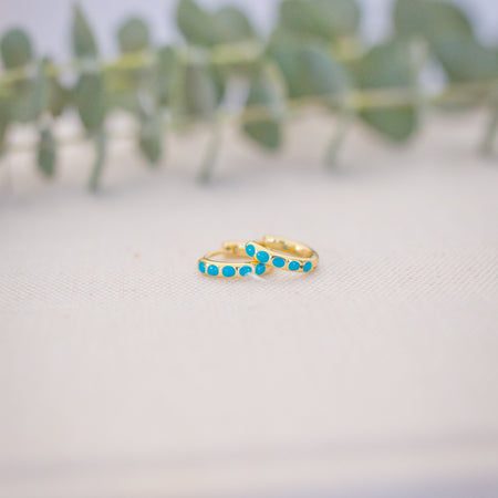 Gold ring with turquoise stones on a textured surface with blurred greenery in the background