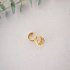 Gold hoop earring on a light gray fabric background with green leaves.