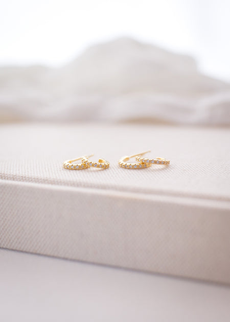 Gold earrings on a white satin surface