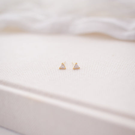 Small gold triangle earrings on a white fabric background