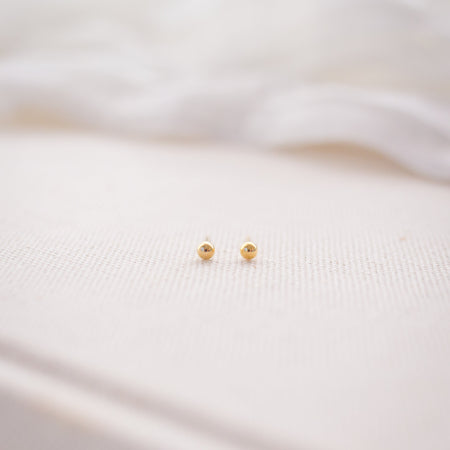 Small gold earrings on a soft pink fabric background