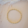 Gold beaded bracelet on a light wooden surface with feathers