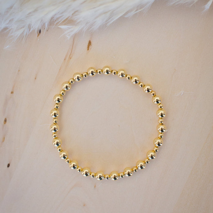 Gold beaded bracelet on a light wooden surface with feathers