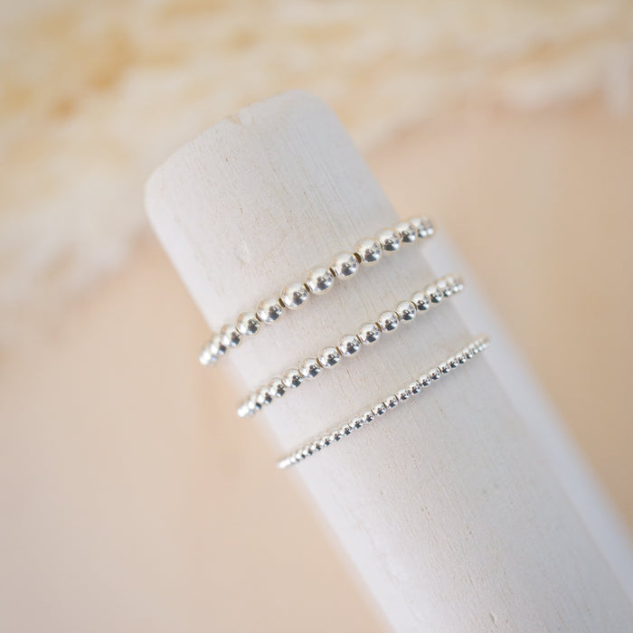 Three silver beaded rings on a white cylindrical stand against a beige background