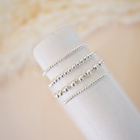 Set of silver beaded rings on a white cylindrical object with a beige background