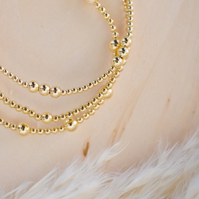 Gold beaded necklace on a textured beige surface