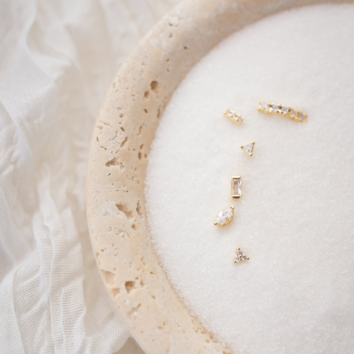 Gold earring set on a white cushion with a light fabric background