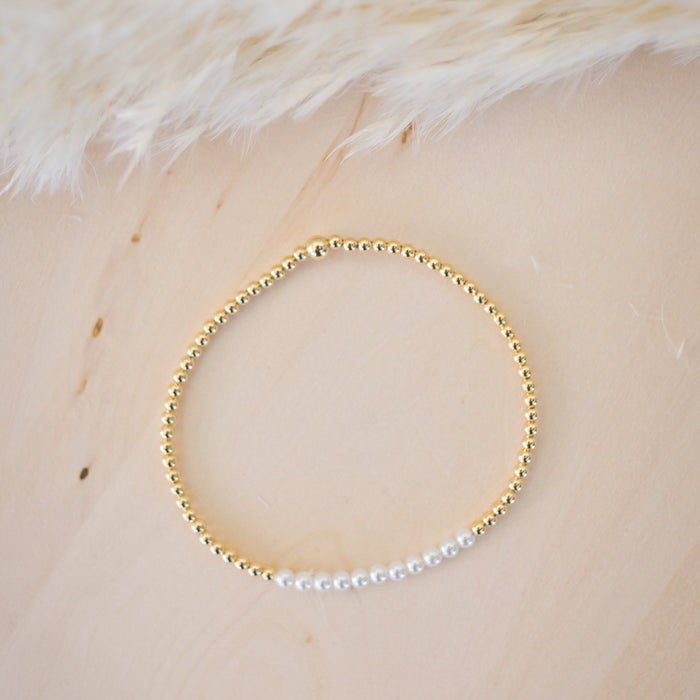 Gold beaded bracelet on a light wooden surface with white feathers in the background