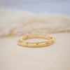 Two gold rings stacked on a textured beige surface with a blurred background