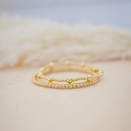 Two gold rings stacked on a textured beige surface with a blurred background