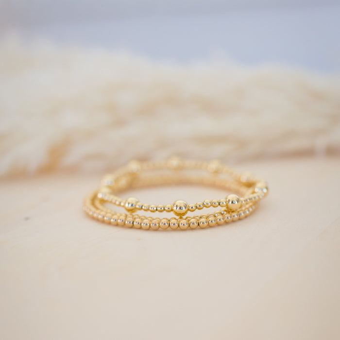 Two gold rings stacked on a textured beige surface with a blurred background