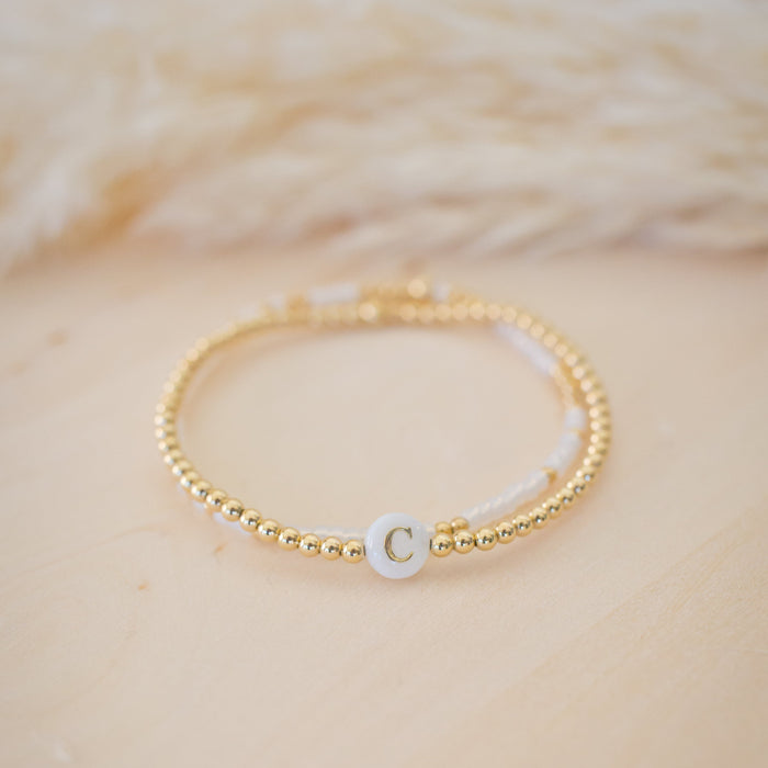 Gold bracelet with a white cord and a small round charm on a beige background