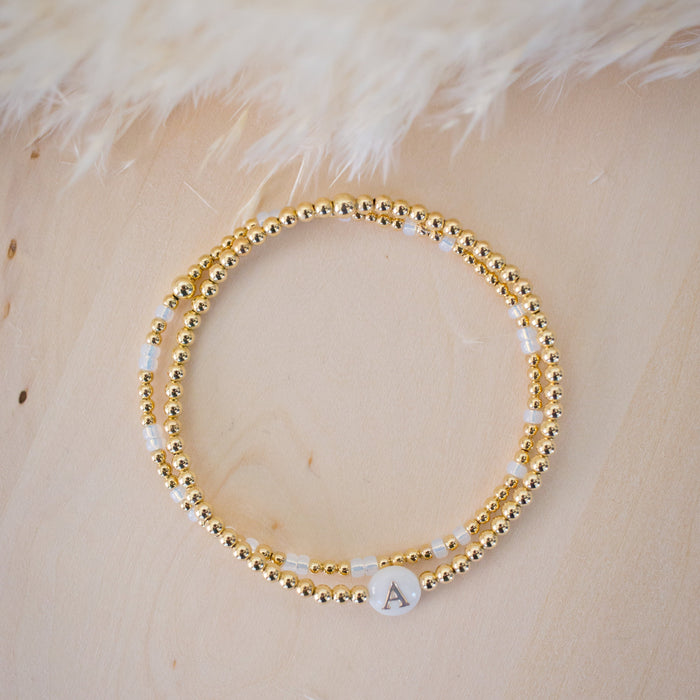 Gold beaded bracelet with a letter 'A' charm on a beige surface
