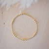 Gold beaded bracelet on a light wooden surface with white feathers