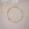 Gold beaded bracelet on a light wooden surface with white feathers