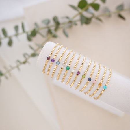 Gold bracelets with colorful beads on a white surface with green leaves in the background