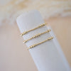 Three gold rings stacked on a white cylindrical stand with a soft beige background