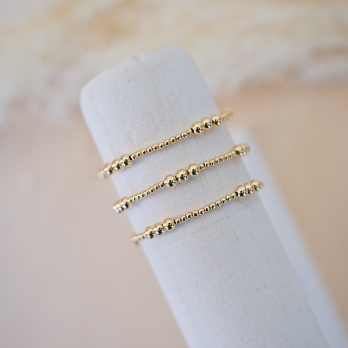 Three gold rings stacked on a white cylindrical stand with a soft beige background