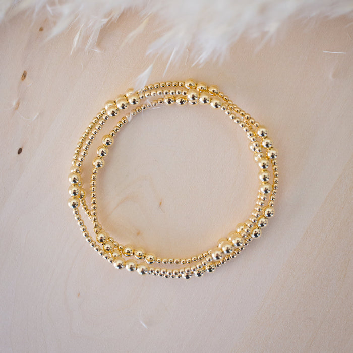 Gold beaded bracelet on a textured beige surface