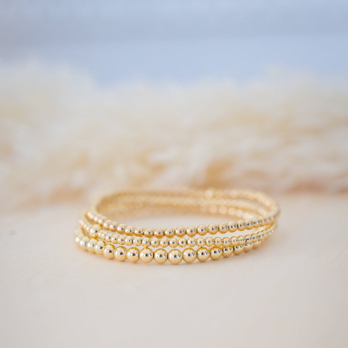 Gold beaded bracelet on a soft beige surface with a blurred background