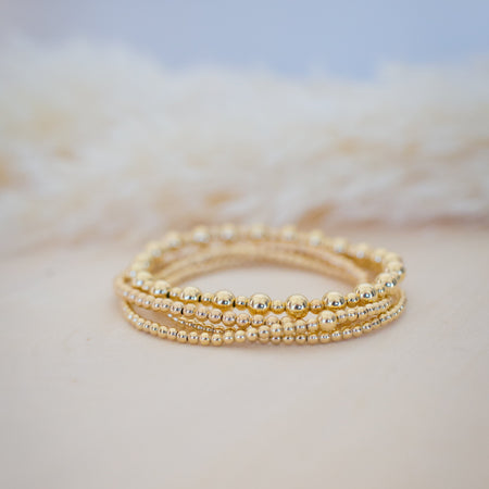 Gold bracelets stacked on a textured beige surface with a blurred blue background