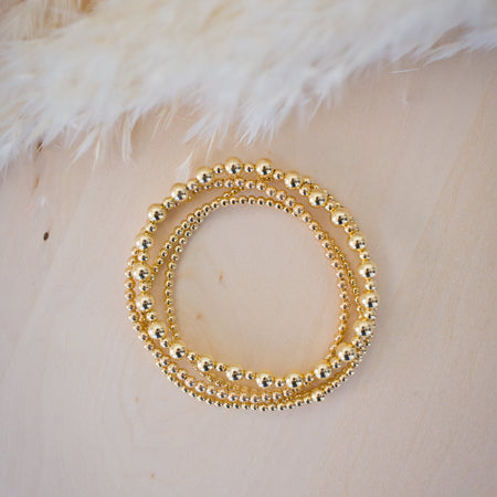 Gold beaded bracelet on a textured beige surface with feathers